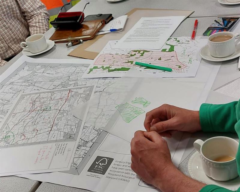 close up of annotated maps, tea cups and hands